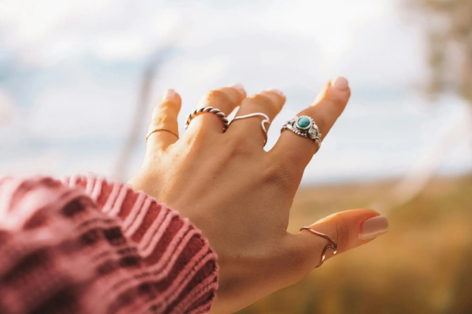 Hand adorned with decorative rings, complemented by a pink burgundy sleeve.