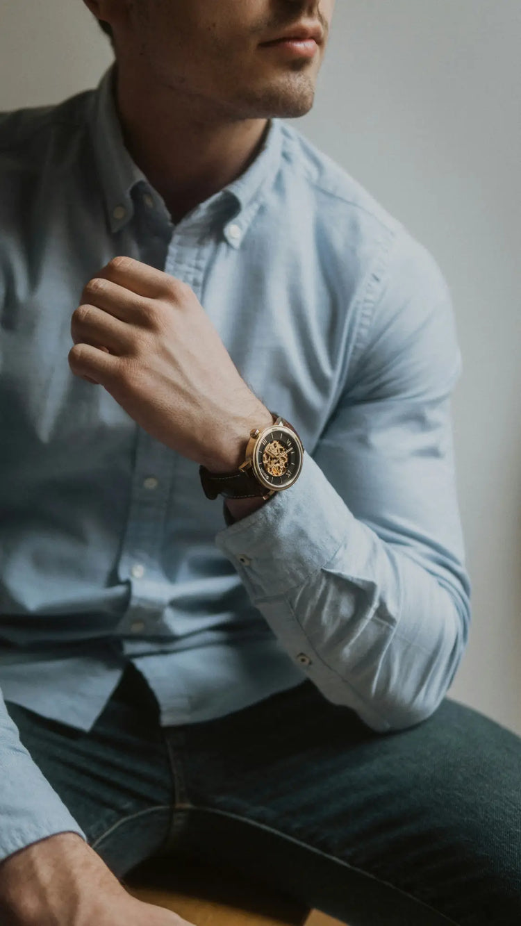 Gold watch paired with light blue button-down shirt in Men’s Watches collection