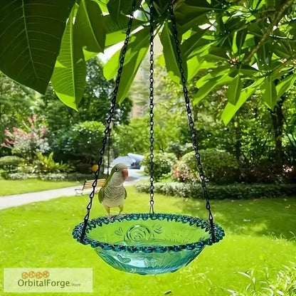 A turquoise glass bird bath hanging by chains beneath green leaves.